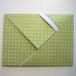 an origami square with white polka dots on green paper and a silver strip