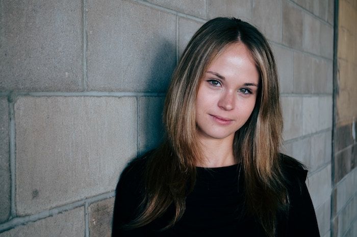 a woman standing next to a brick wall with her eyes closed and looking at the camera