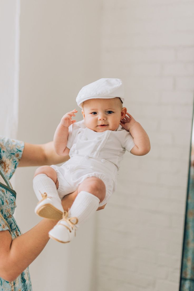 a woman holding a baby up to her ear while she is wearing a white hat