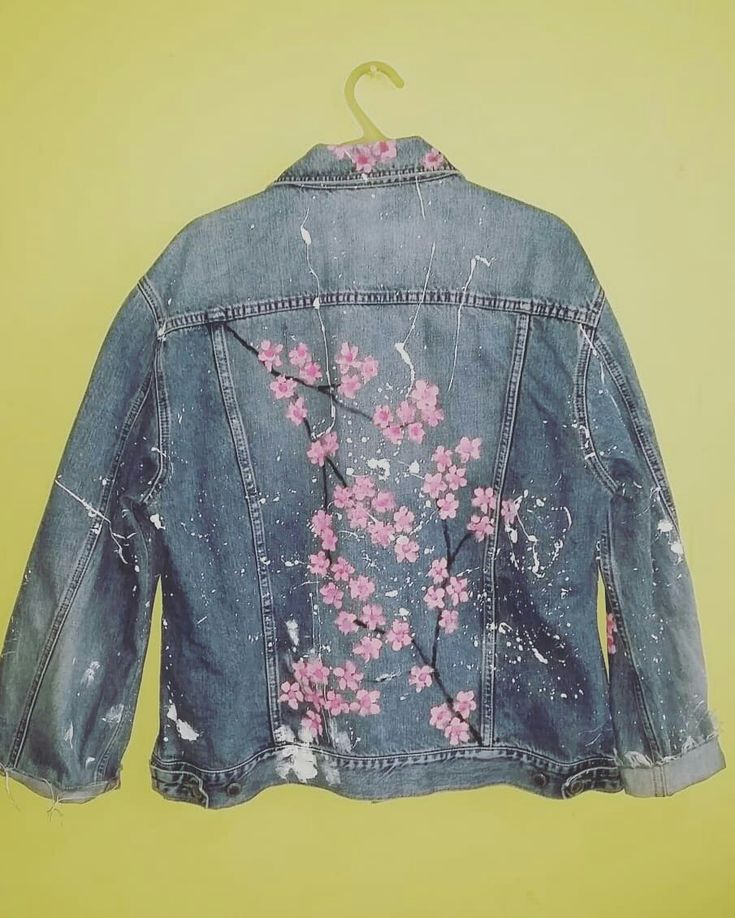 a denim jacket with pink flowers painted on it and a hanger attached to the back