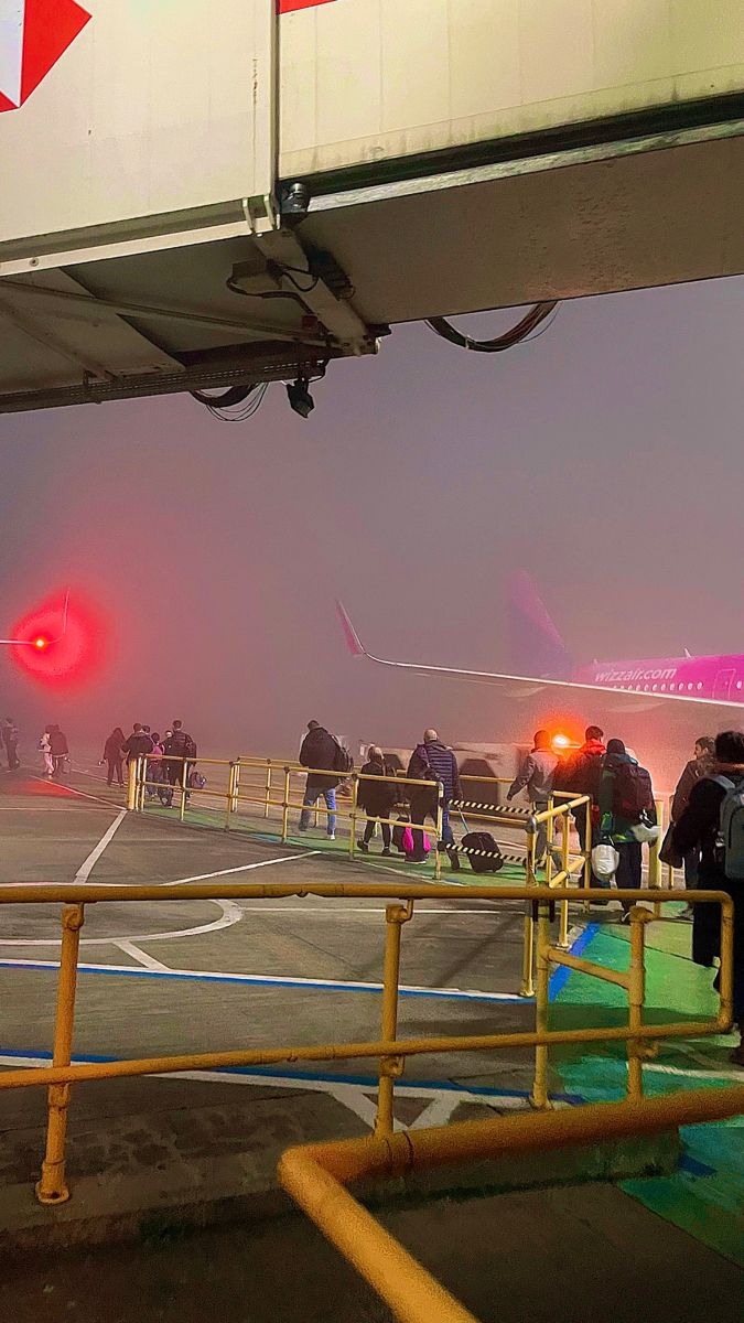 several people are standing on the deck of an airplane at night with red lights in the background