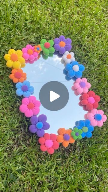 a flower shaped mirror sitting on top of a green grass covered field with flowers in the middle