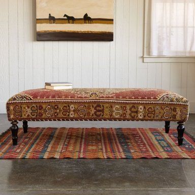 a bench sitting on top of a rug in front of a painting hanging on the wall