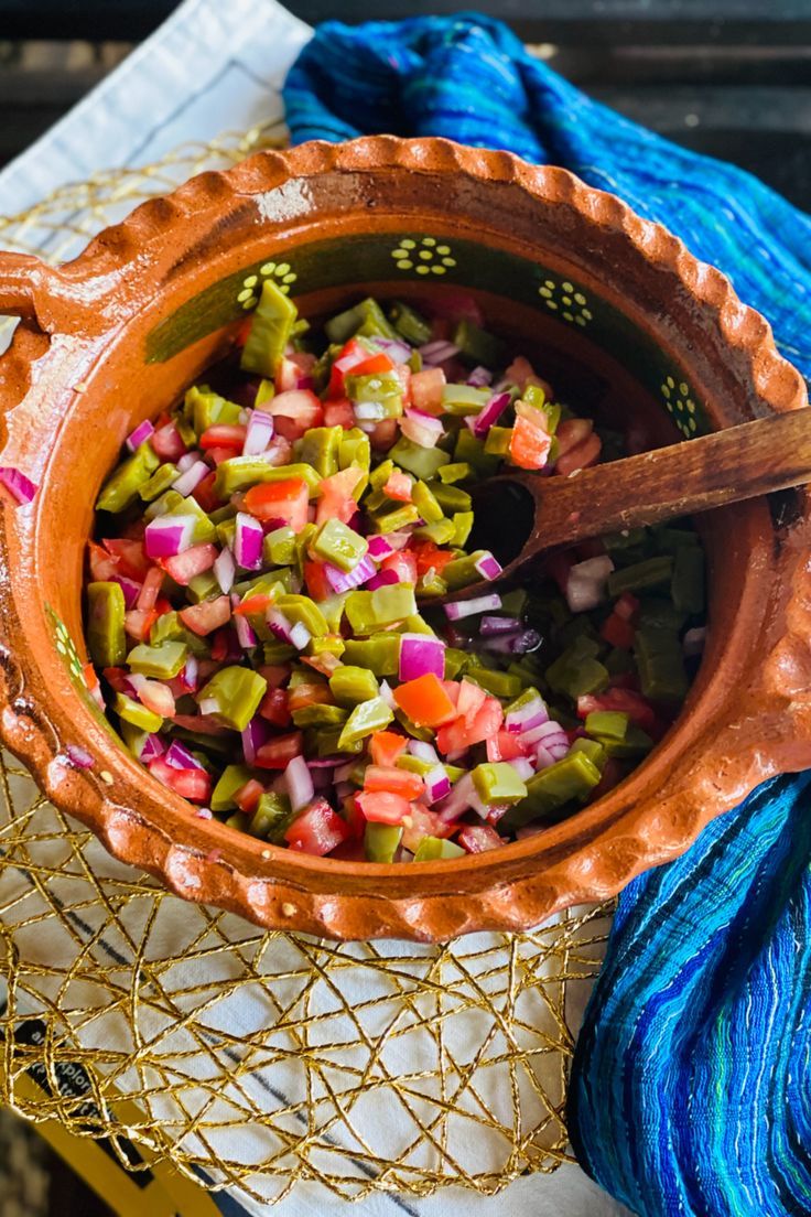 a bowl filled with chopped vegetables on top of a table next to blue yarn and a wooden spoon