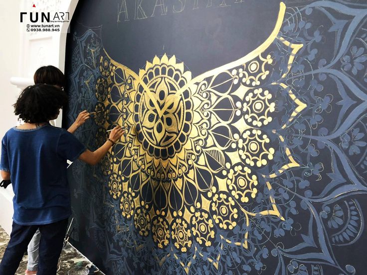 two people are painting the side of a wall with gold designs on it and another person is standing next to them