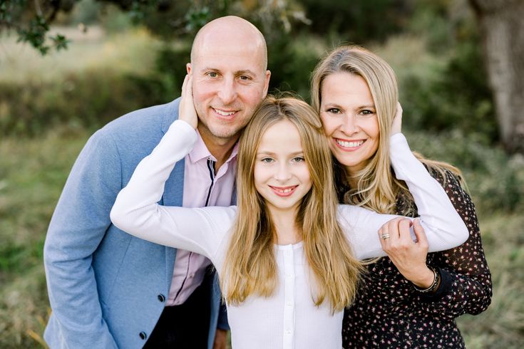 a man and two women pose for a photo in front of some trees with their arms around each other