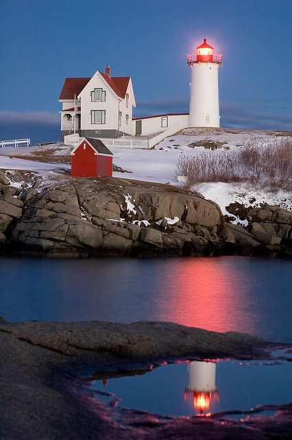 a light house on top of a snowy hill next to a body of water at night