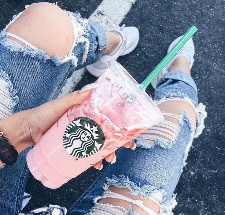 a woman is holding a starbucks drink in her hand while sitting on the curb with ripped jeans