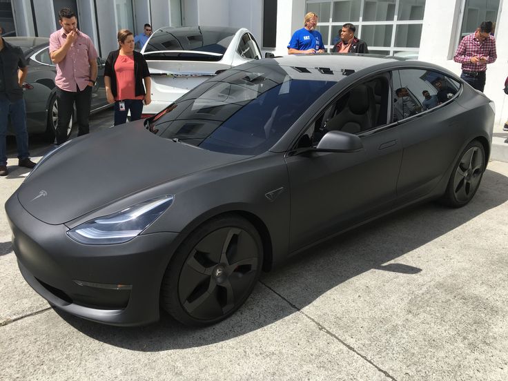 people are standing around and looking at an electric car