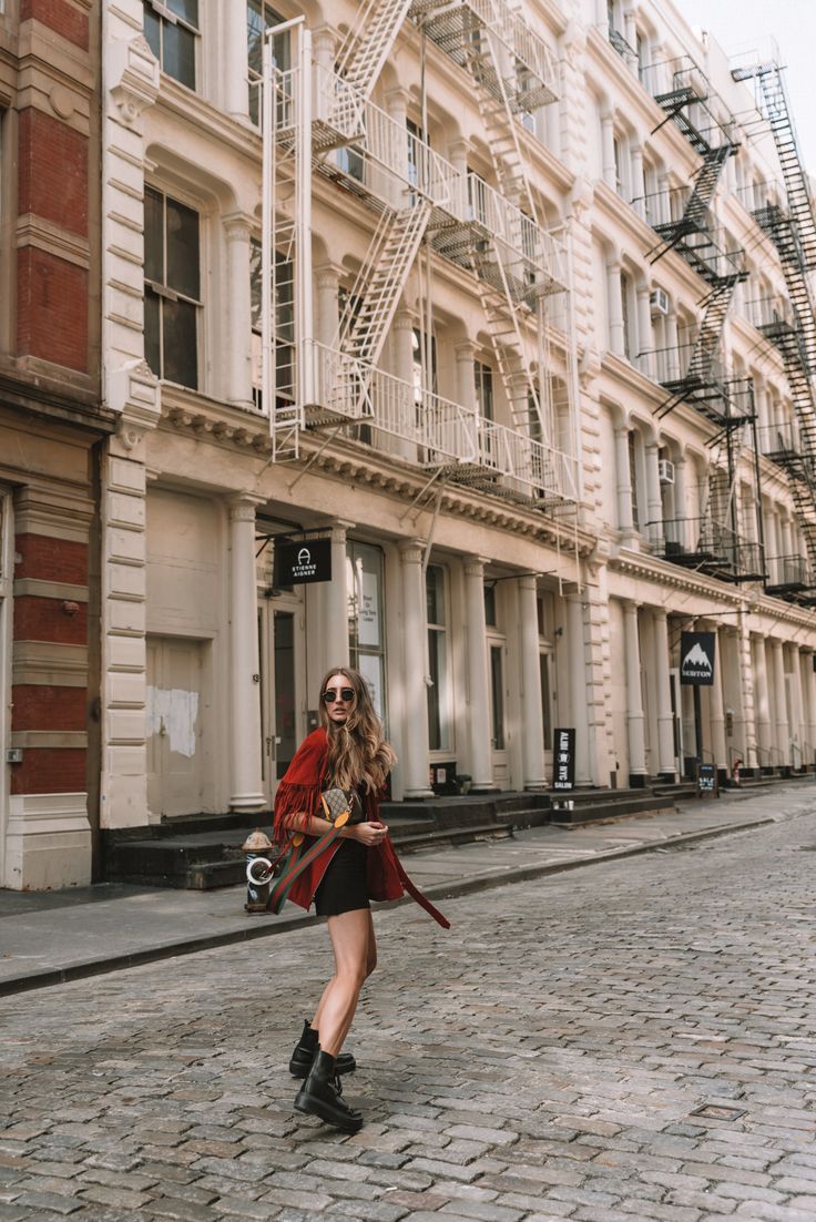 a woman is walking down the street with a camera in her hand and wearing boots