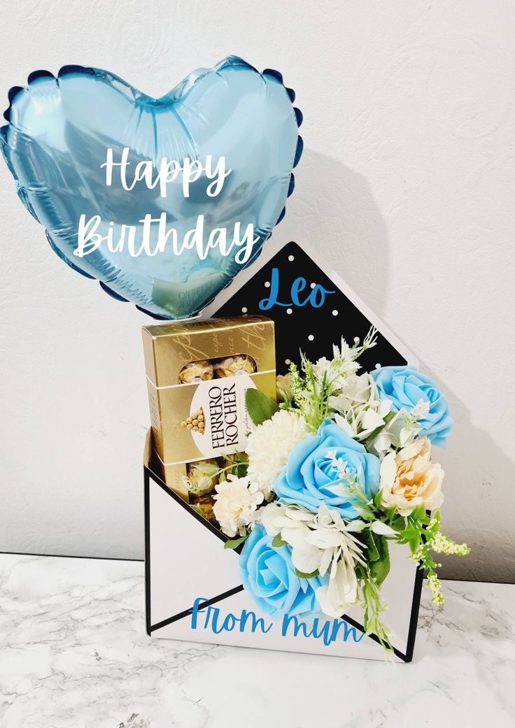 a blue heart shaped balloon sitting on top of a box filled with flowers