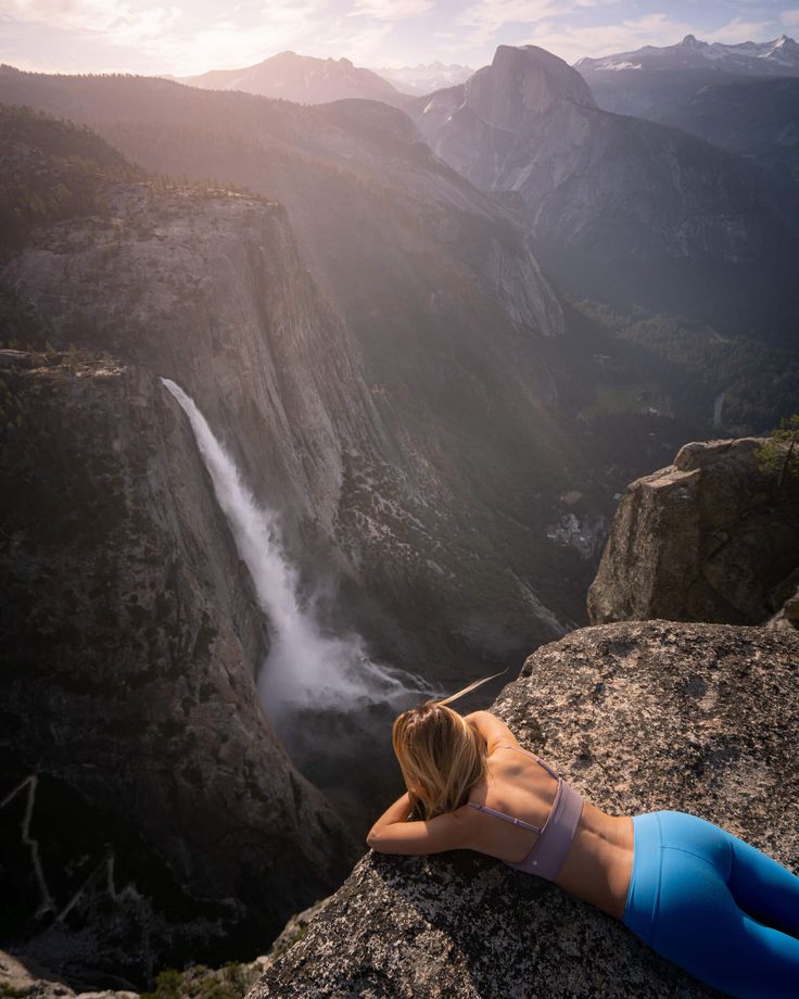 a woman laying on top of a cliff next to a waterfall