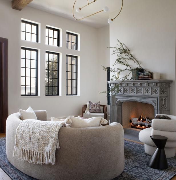 a living room filled with furniture and a fire place in front of a windowed wall