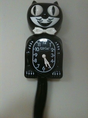 a black clock with a cat face on it's face is hanging from the wall