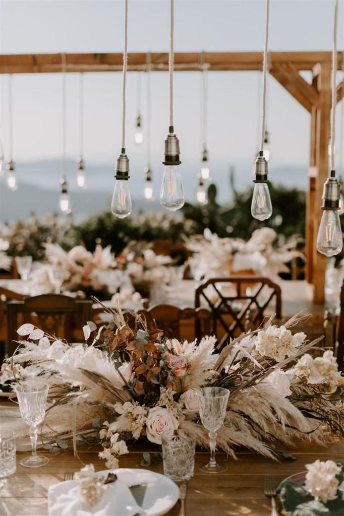 the table is set with white flowers and hanging light bulb chandeliers, which are hung from wooden beams