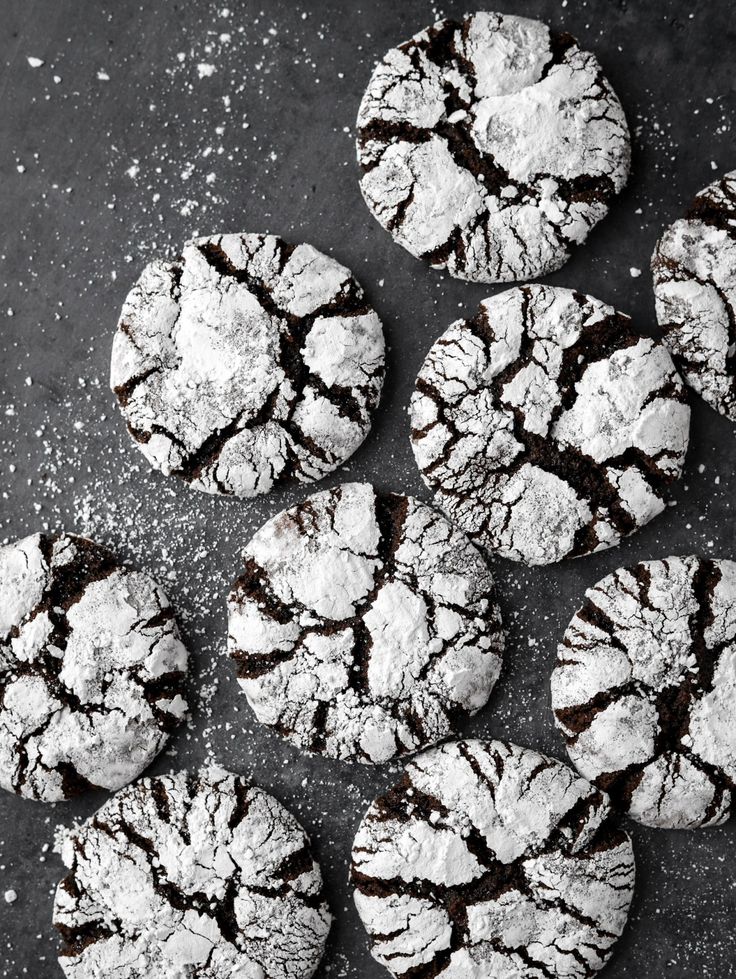 chocolate crinkle cookies on a black surface with powdered sugar and sprinkles