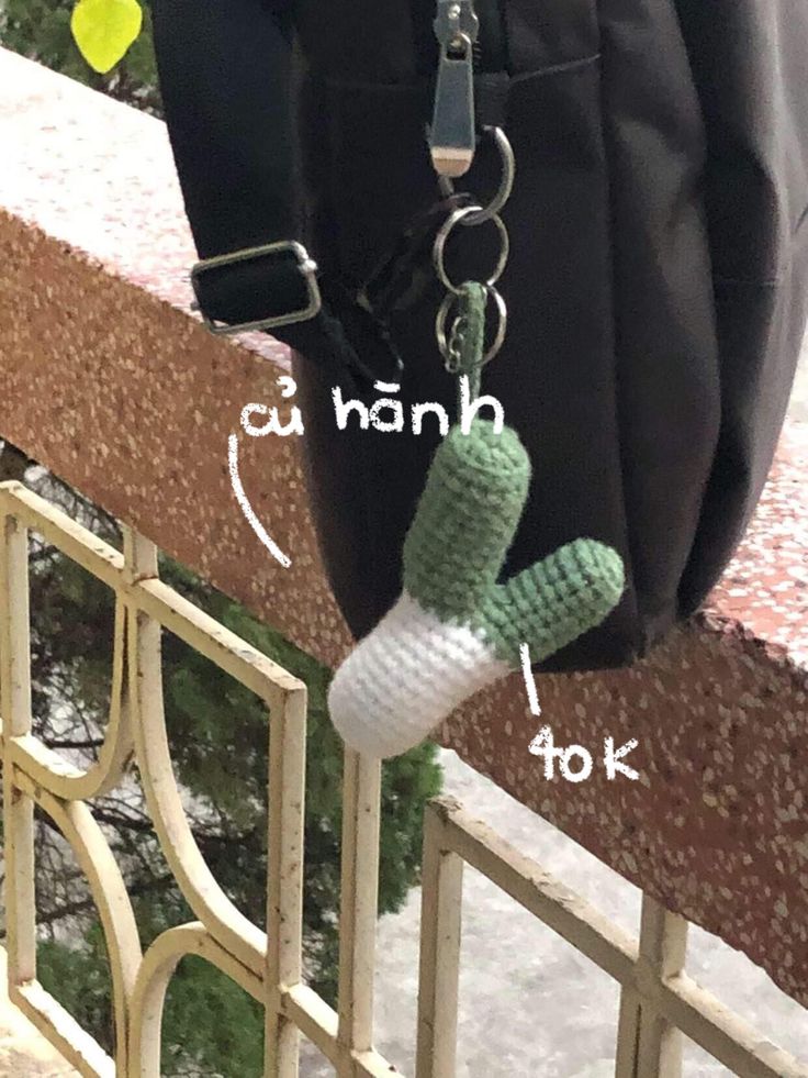 a crocheted cactus keychain attached to a handbag hanging on a railing