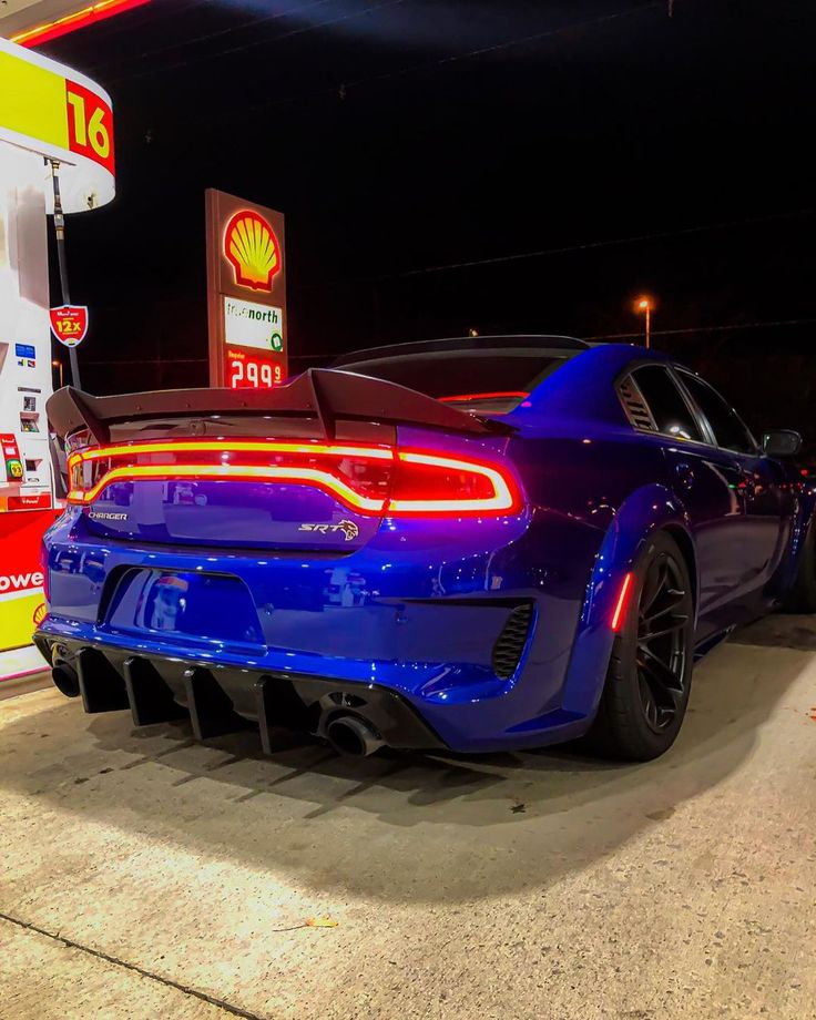 a blue sports car is parked in front of a gas station at night with the lights on