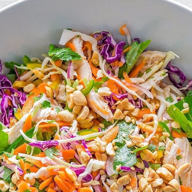 a salad with chicken, carrots and lettuce in a white bowl