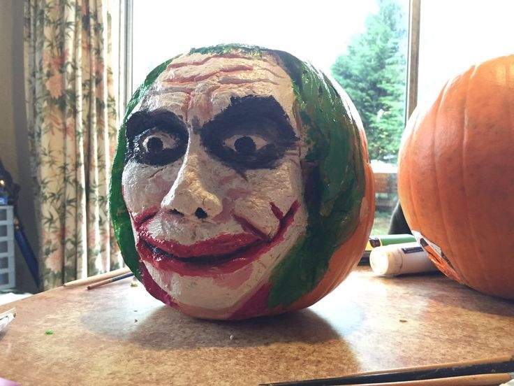 a pumpkin with a face painted to look like it is sitting on a table next to a window