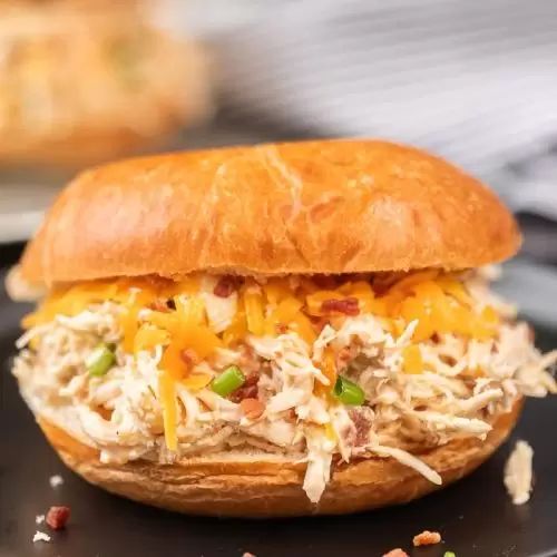 a close up of a chicken sandwich on a plate with other food items in the background