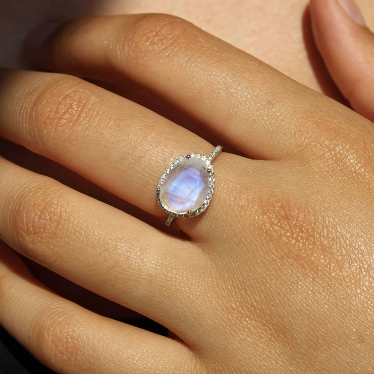 Introducing the Skye Moonstone Ring—a classic piece that features a genuine Rainbow Moonstone, beautifully framed by a halo of sparkling crystals on a pave band. Choose between luxurious 14k Gold Vermeil or elegant Sterling Silver, and let this naturally stunning gemstone captivate you with its unique charm. Each Rainbow Moonstone is handpicked for its individual beauty, ensuring that your ring is truly one-of-a-kind. Details:Gemstone: 9x11mm Genuine Rainbow MoonstoneRing Face (including crystal Cheap Oval Crystal Ring, Elven Accessories, Country Necklace, Gold Moonstone Ring, Pave Band, Rainbow Moonstone Ring, Moonstone Jewelry, Pretty Rings, Moonstone Ring