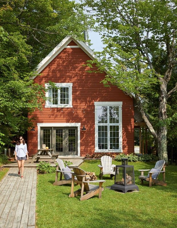 a woman walking past a red house with lawn chairs on the front and back yard