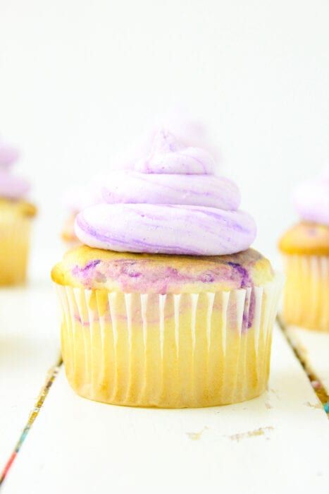 cupcakes with purple frosting and sprinkles sitting on a table