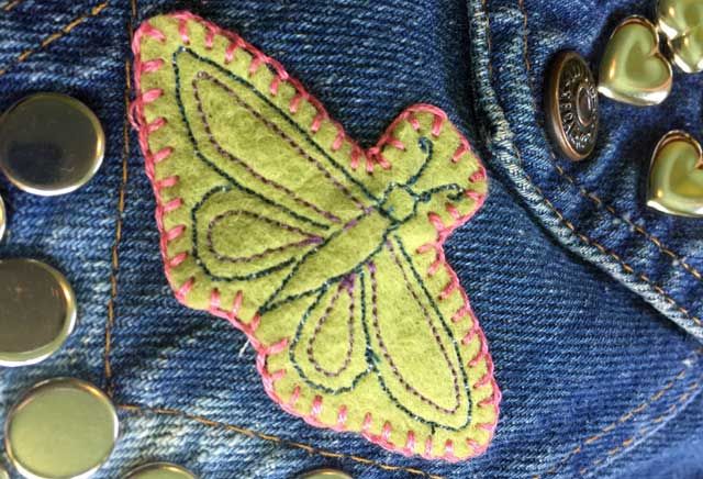 a butterfly patch is on the back of a pair of blue jeans with buttons and sequins