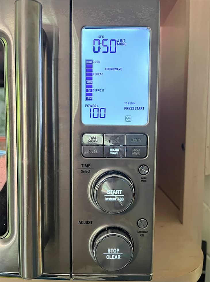 a digital clock on the side of a stainless steel microwave oven with its door open