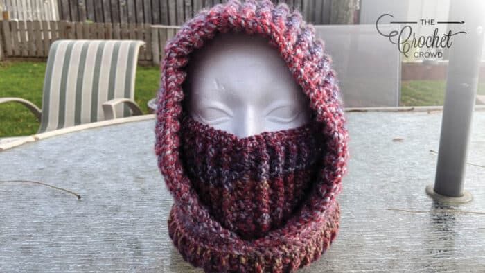 a crocheted hat with a hood on top of it sitting on a table