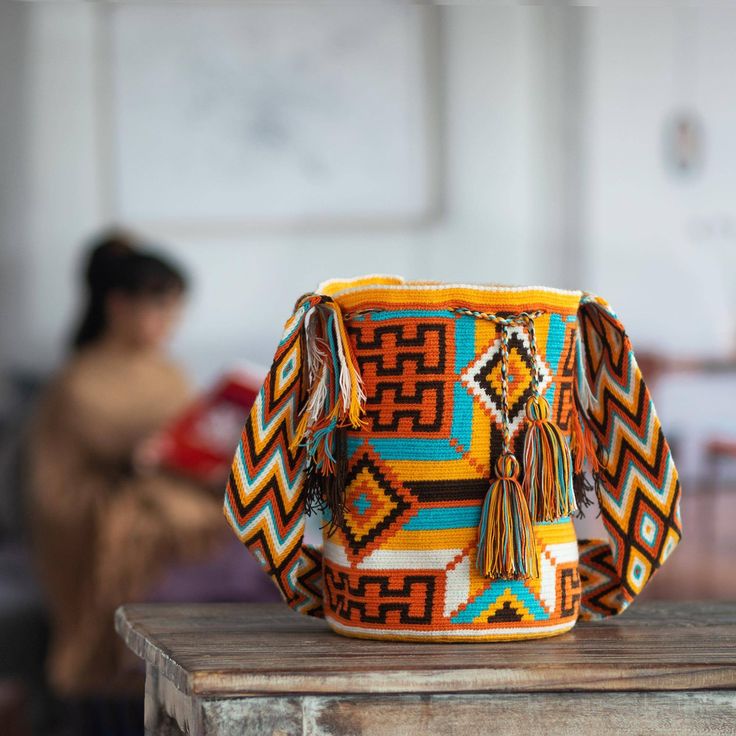 Bold patterns in orange brown blue and white are captivating in this hand-crocheted acrylic bucket bag or mochila. Working to preserve their cultural identity and artisanal traditions artisans of the Wayuu Community create the shoulder bag. The Wayuu are an indigenous people located on the Guajira Peninsula in northern Colombia. Legend has it that a spider named Wale Keru taught a Wayuu woman how to weave and crochet. The unlined shoulder bag closes with a tassel-accented drawstring. How To Weave, Caribbean Culture, Heritage Crafts, Surrealist Art, Crochet Shoulder Bag, Tapestry Crochet Patterns, Amazing Crochet, Wayuu Bag, Woven Handbags