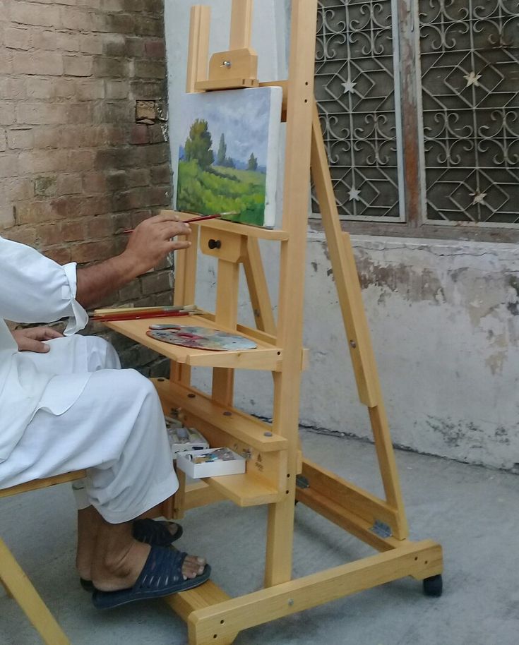 a man sitting in front of an easel with a painting on the easel