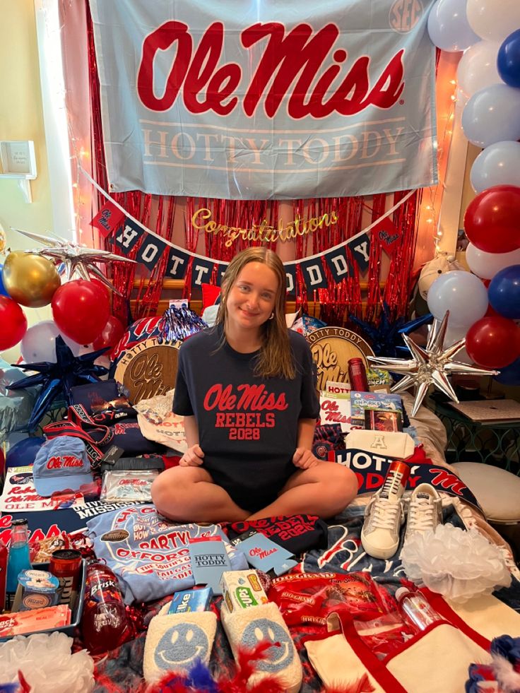 a woman sitting on the floor surrounded by cake and balloons in front of a banner