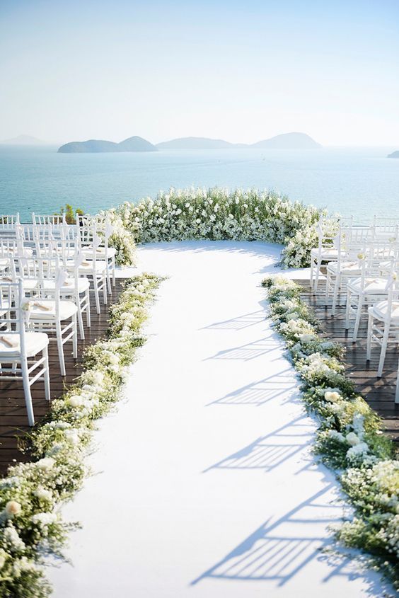 an outdoor ceremony setup with white chairs and flowers on the aisle, overlooking the ocean