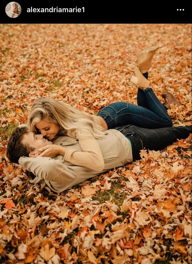 a man and woman laying on the ground covered in leaves with their arms around each other