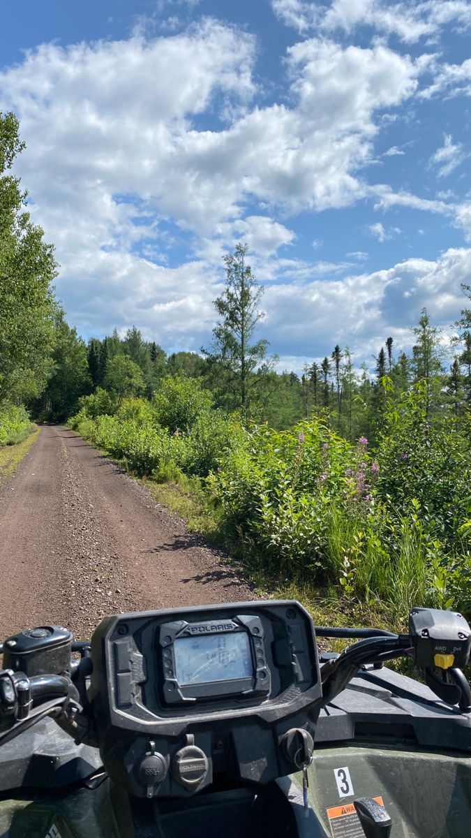 a motorcycle is parked on the side of a dirt road with trees and bushes in the background