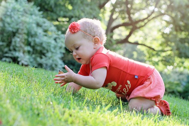 a baby girl crawling in the grass with her hands out to touch it's fingers