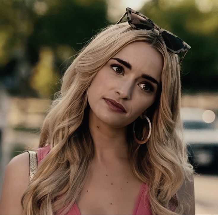 a woman with long blonde hair and large hoop earrings on her head looking at the camera