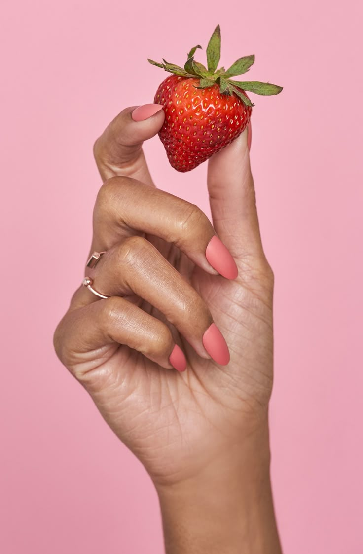 a woman's hand holding a strawberry up to the camera with her fingers on it