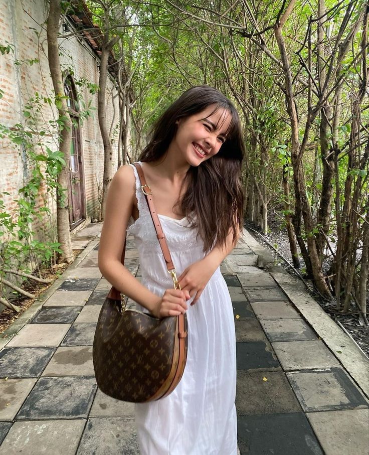 a woman in a white dress is holding a brown purse and smiling at the camera