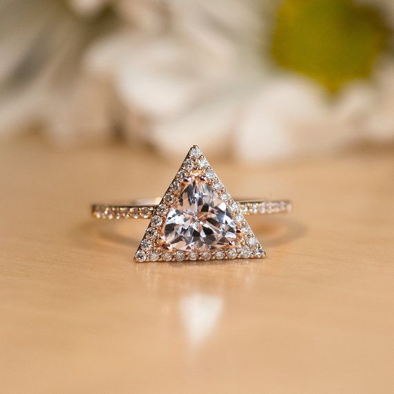 a triangle shaped diamond ring sitting on top of a wooden table with white flowers in the background