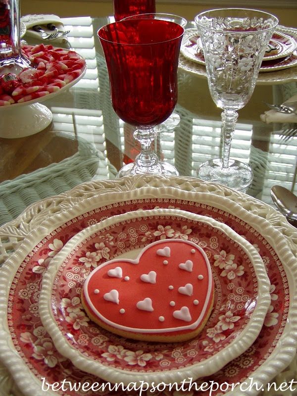 a heart shaped cookie sitting on top of a red and white plate next to wine glasses