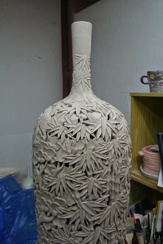 a white vase sitting on top of a table next to a wooden shelf filled with books