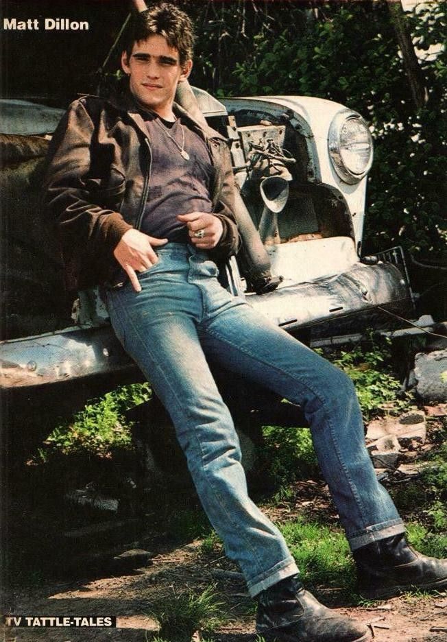 a young man sitting on the hood of an old truck with his feet propped up