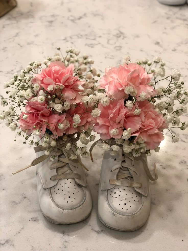 two baby's shoes with flowers in them sitting on a marble counter top,