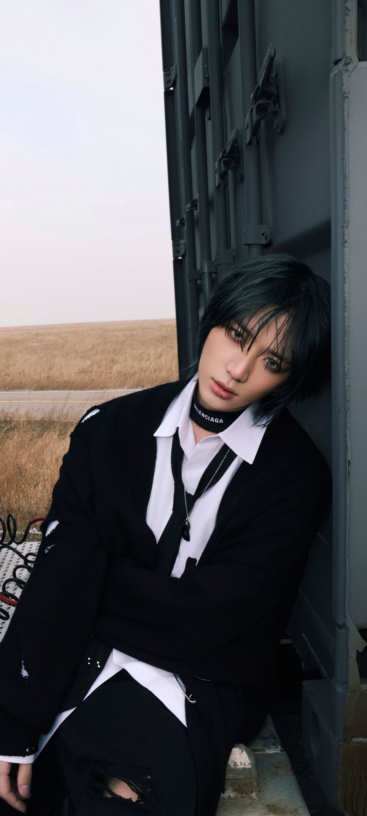 a man with black hair wearing a suit and tie sitting in front of a door