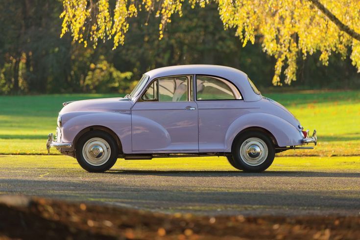 an old purple car is parked on the side of the road in front of some trees