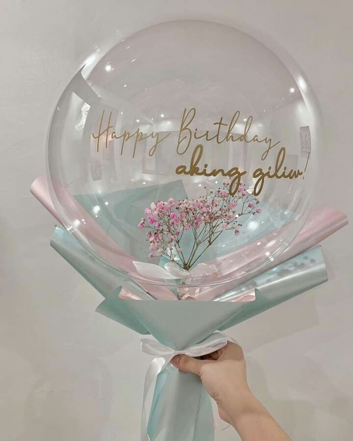 a person holding a clear balloon with flowers in it and the words happy birthday along side