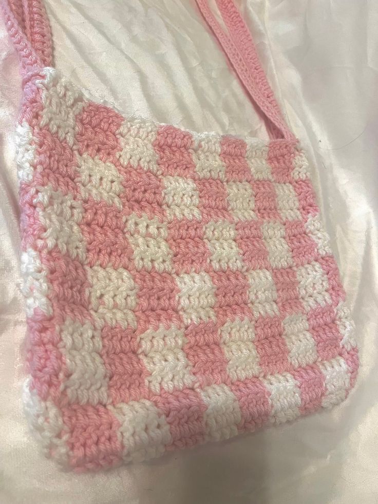 a pink and white crocheted purse sitting on top of a bed next to a pillow